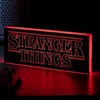 A Stranger Things logo light is displayed on a dark surface, casting a red glow. Produktbild-Vorschau