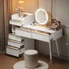 A white vanity table with gold accents and a lighted mirror, set up in a room with curtains and decorative elements. Produktbild-Vorschau