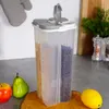 A multi-compartment food storage container filled with coffee beans and cereal, placed on a kitchen counter with fruit and kitchenware in the background. Produktbild-Vorschau