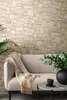 A cozy living room scene with a sofa, blanket, and plants, set against a stone wall. Náhľad obrázku produktu
