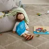 A plush doll of Jesus sitting on a carpeted floor next to a beanbag chair and toys. Produktbild-Vorschau