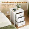 A white bedside table with three drawers, one of which is open, is shown next to a bed. A phone is charging on top of the table. Podgląd zdjęcia produktu