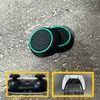 Two black and green thumbstick grips for a game controller are shown on a textured gray surface. Insets show the bottom of a black controller and a white controller with colored thumbstick caps. Produktbild-Vorschau