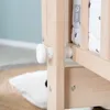 Close-up of a wooden baby crib with a white knob and a patterned fabric lining. Produktbild-Vorschau