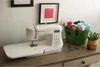 A sewing machine is displayed on a wooden desk with sewing supplies. Produktbild-Vorschau