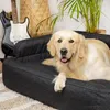 A golden retriever dog is lying on a dark gray dog bed in a room with a guitar and a plant in the background. Náhľad obrázku produktu