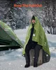 A man is sitting on a log wrapped in a green blanket in a snowy forest with a tent nearby. Anteprima dell’immagine prodotto