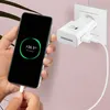 A hand holding a smartphone that is charging, with a Samsung charger plugged into a wall socket. Produktbild-Vorschau