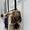 Brauner Stoffrucksack mit silbernem ineinandergreifendem Logo, hängend an einem Kleiderständer in einem Geschäft Anteprima dell’immagine prodotto