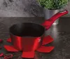 A red pot sits on a dark countertop, with a plant in a silver pot in the background. Náhled obrázku produktu