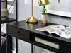A close-up view of a black desk with a lamp, a plant, and an open magazine. Voir les images du produit