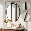 A round black framed mirror is shown above a bathroom vanity with a gold faucet and flowers in a vase. Podgląd zdjęcia produktu