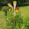 A decorative bee-shaped wind spinner is placed in a garden setting. Produktbild-Vorschau