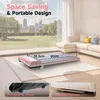 A pink and white treadmill is shown on a cream rug in a living room with a large window overlooking a city. Produktbild-Vorschau