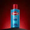 A bottle of Alpecin shampoo is displayed on a black surface against a red gradient background. Anteprima dell’immagine prodotto