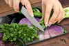 A person is chopping green onions on a glass cutting board with an orchid design. Náhľad obrázku produktu
