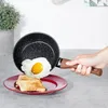 A hand is holding a frying pan with a fried egg over toast on a plate. Podgląd zdjęcia produktu