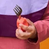 A child's hand holding a fork with an orange handle. Voir les images du produit