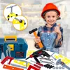 A young child wearing a hard hat and overalls, holding a toy hammer and giving a thumbs up, surrounded by toy tools and a toolbox. Produktbild-Vorschau