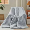 A light gray plush blanket is draped over a chair in a room with blinds and a plant. Produktbild-Vorschau