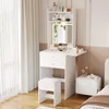 A white vanity table with a mirror and stool, set up in a bedroom next to a window and a nightstand.