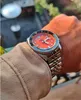 A person's wrist wearing a Seiko 5 Sports GMT watch with an orange dial, set against an outdoor background. Podgląd zdjęcia produktu
