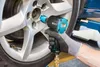 A person is using an impact wrench to remove a lug nut from a car wheel. Produktbild-Vorschau