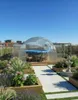 A rooftop garden with a greenhouse covering a hot tub, surrounded by plants and a fountain. Produktbild-Vorschau