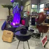 A retail store display featuring various grilling accessories, including a large statue of liberty replica, bags of charcoal, and several grills. Produktbild-Vorschau