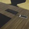 A close-up view of a wooden conference table with a black pop-up power outlet and a smartphone connected to it. Produktbild-Vorschau