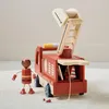 A wooden toy fire truck with a firefighter figurine and accessories on a carpeted floor. Produktbild-Vorschau