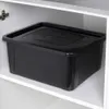 A black storage box with a lid sits inside a white cabinet. Produktbild-Vorschau