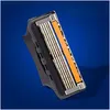 A close-up of a razor blade head with multiple blades and an orange lubrication strip, set against a solid blue background. Produktbild-Vorschau