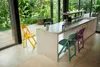 A modern kitchen area with a concrete island and chairs, opening up to a lush green outdoor space. Produktbild-Vorschau