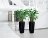 Two large black planters with green plants inside, placed in a modern, well-lit interior with a staircase and glass railings. Produktbild-Vorschau