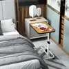 A mobile bedside table with a laptop and snacks is placed next to a bed in a bedroom. Produktbild-Vorschau