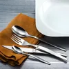 A set of cutlery laid out on a napkin on a wooden surface, with a white plate in the background. Anteprima dell’immagine prodotto