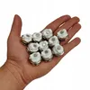 A hand holding a collection of small, white and silver radiator vent valves. Podgląd zdjęcia produktu