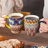 Zwei Hände halten bunt Tassen mit Kaffee über einem Holz Tisch, auf dem Brot und Croissants liegen. Náhled obrázku produktu