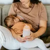 A person is breastfeeding a baby while holding a baby bottle. Anteprima dell’immagine prodotto