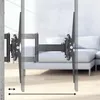 A TV wall mount is shown extended from a wall, demonstrating its adjustable reach. The background shows a blurred living room with a sofa. Voir les images du produit