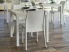 A white rattan dining set with chairs and a table, set on a wooden floor, likely in an outdoor or patio setting. Produktbild-Vorschau