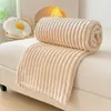 A rolled-up beige blanket is placed on a white surface, possibly a bed or sofa. A pillow shaped like a fried egg is visible in the background. Náhled obrázku produktu