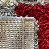 A close-up view of a shaggy rug with a checkered pattern in red, gray, and cream colors. The image shows the texture and weave of the rug. Produktbild-Vorschau