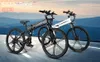 Two electric bicycles are displayed on a road with a blurred mountainous background. Produktbild-Vorschau