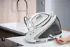 A steam iron and its base unit are placed on a countertop next to a sink, with a hand inserting a red tool into the base. Produktbild-Vorschau