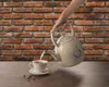A hand is pouring hot water from a cream-colored electric kettle into a white teacup, set against a brick wall background. Anteprima dell’immagine prodotto