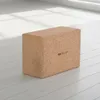 A cork yoga block is placed on a light-colored wooden floor in a room with natural light coming from a window. Produktbild-Vorschau