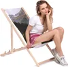 A young woman is sitting on a foldable deck chair with a mountain landscape printed on the fabric. Produktbild-Vorschau