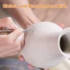 A person's hands are shown sculpting a clay vase with a tool. Produktbild-Vorschau